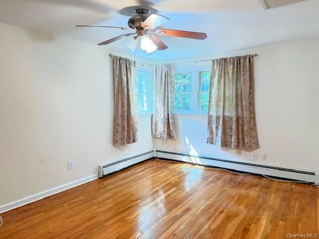 Unfurnished room with wood finished floors, a baseboard heating unit, and a ceiling fan Unfurnished room with wood finished floors, a baseboard heating unit, and a ceiling fan
