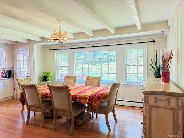 Dining area featuring beam ceiling, light wood-style floors, a chandelier, and a baseboard radiator Dining area featuring beam ceiling, light wood-style floors, a chandelier, and a baseboard radiator