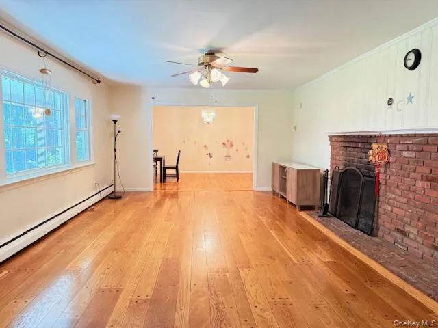 Unfurnished living room with light wood-style floors, a brick fireplace, a baseboard radiator, and ceiling fan Unfurnished living room with light wood-style floors, a brick fireplace, a baseboard radiator, and ceiling fan
