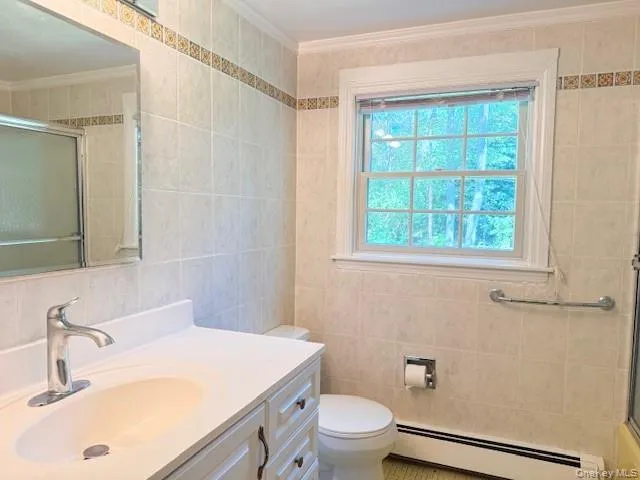 Full bath featuring baseboard heating, a shower stall, vanity, tile walls, and ornamental molding Full bath featuring baseboard heating, a shower stall, vanity, tile walls, and ornamental molding