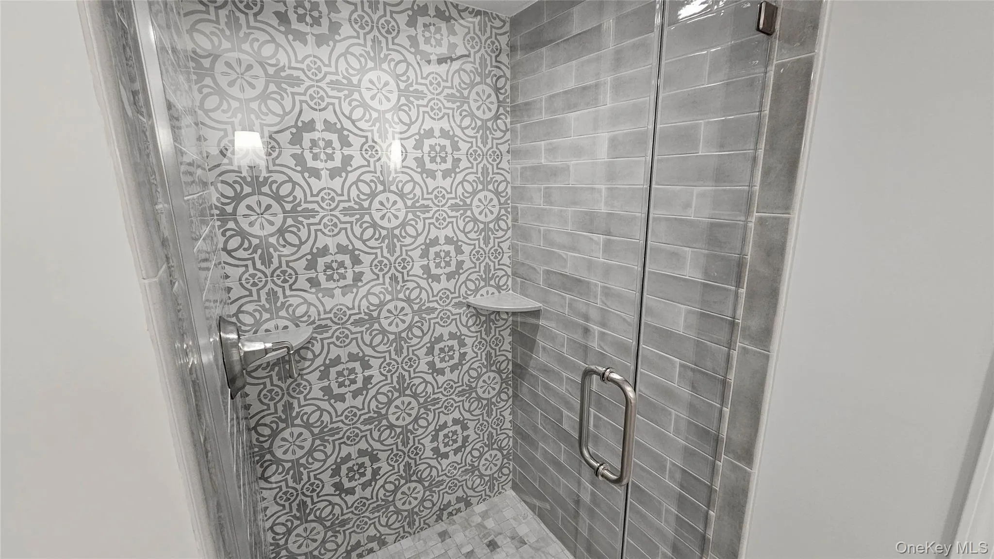 Newly renovated bathroom with glass enclosed shower with tile walls and flooring Newly renovated bathroom with glass enclosed shower with tile walls and flooring