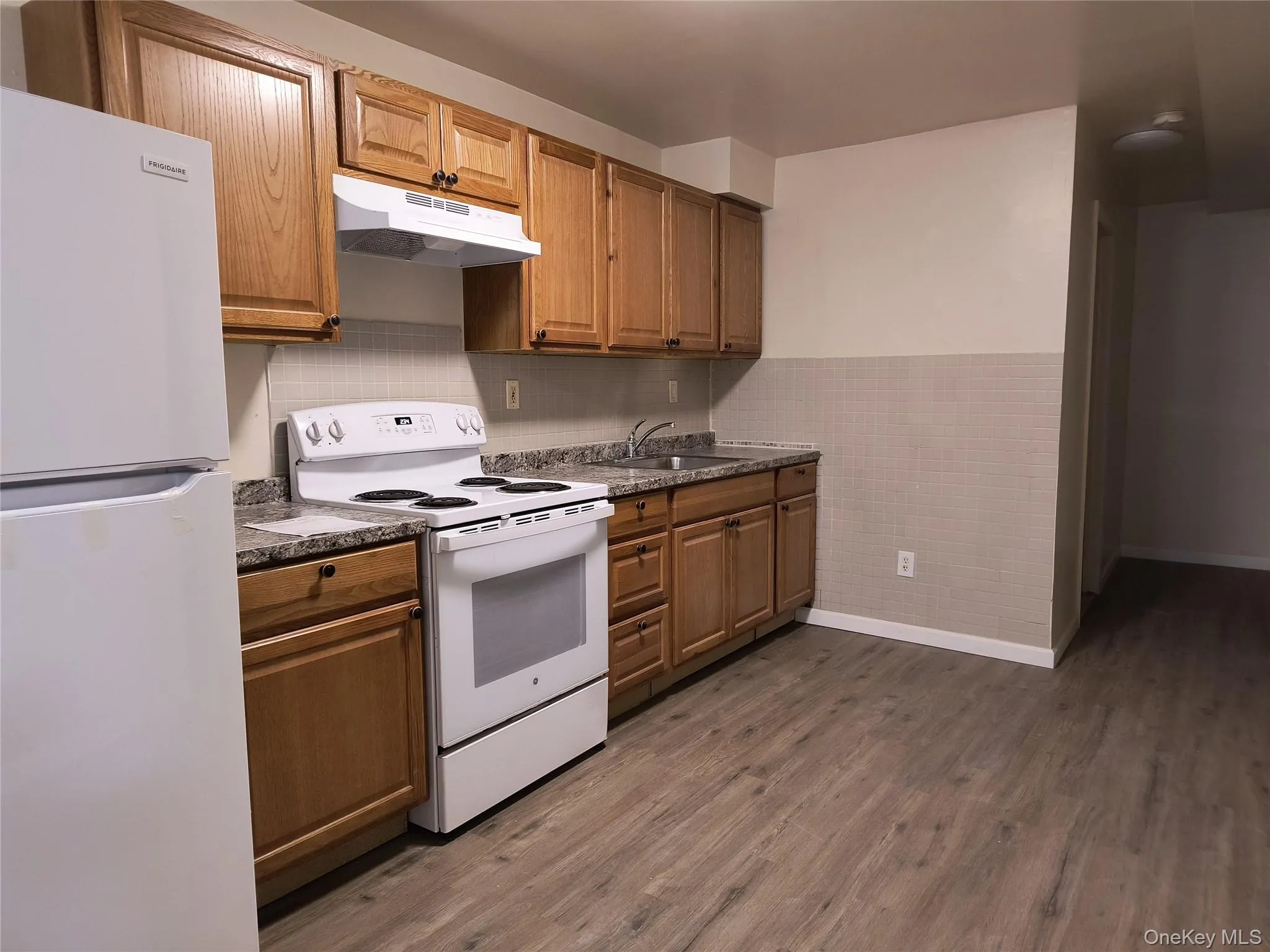 Kitchen featuring white appliances, under cabinet range hood, dark floors, brown cabinets, and wainscoting Kitchen featuring white appliances, under cabinet range hood, dark floors, brown cabinets, and wainscoting