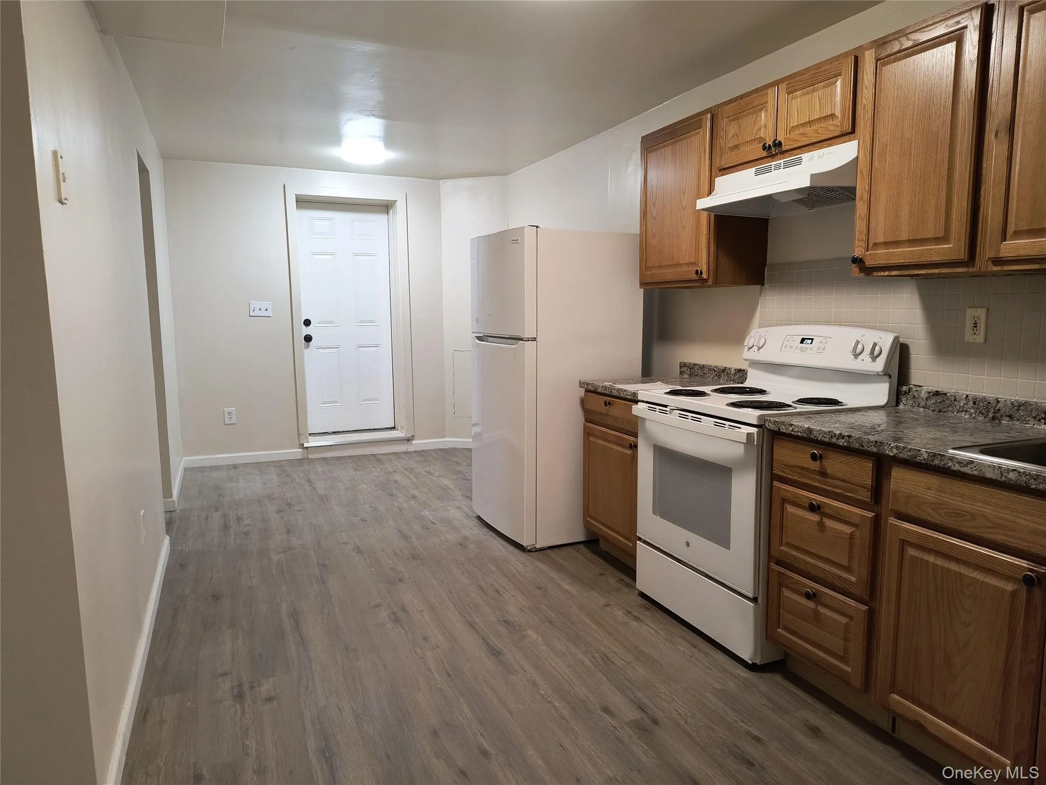 Kitchen with under cabinet range hood, white appliances, dark floors, dark countertops Kitchen with under cabinet range hood, white appliances, dark floors, dark countertops