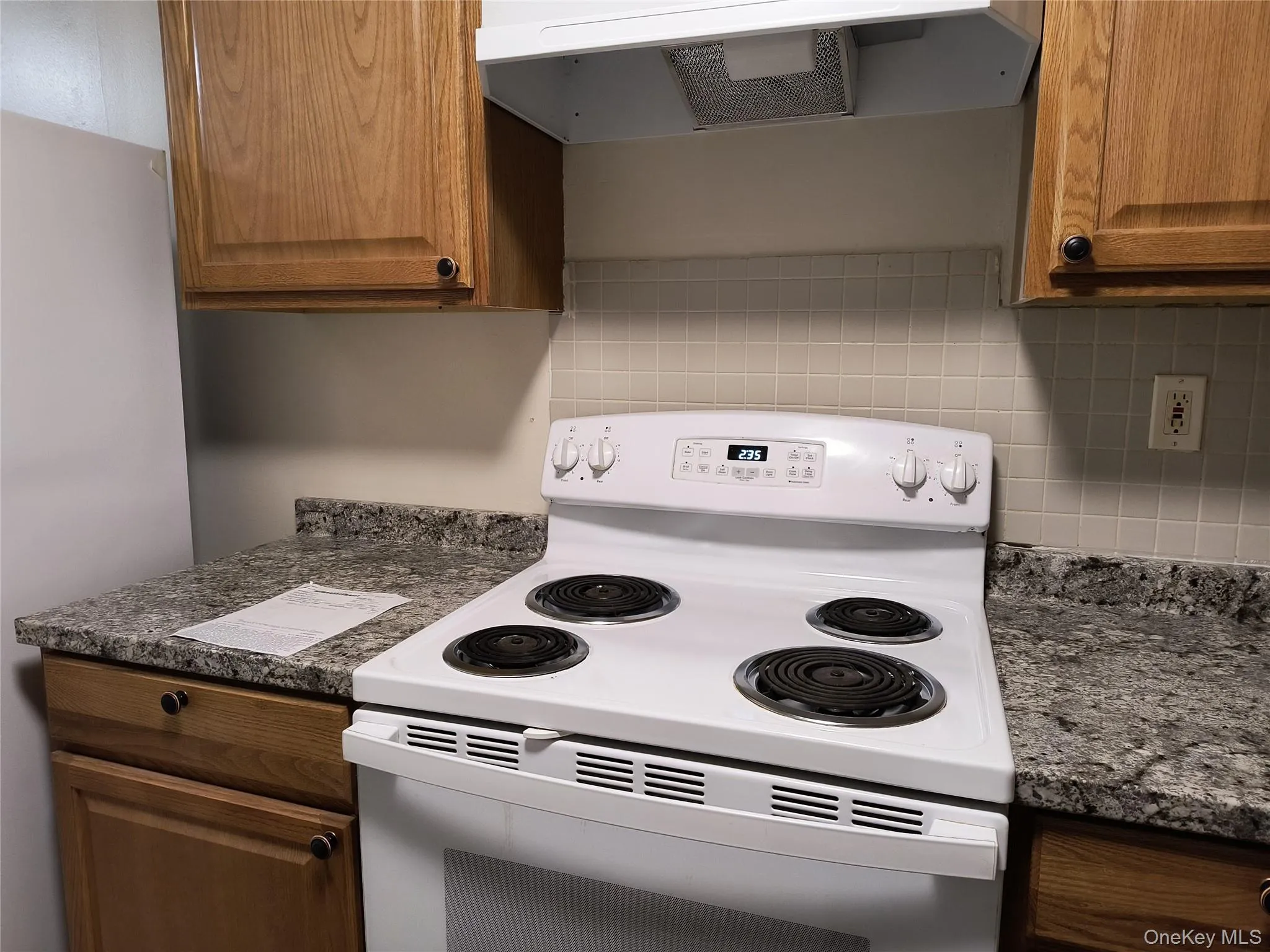 Kitchen featuring electric range, ventilation hood, freestanding refrigerator, and brown cabinetry Kitchen featuring electric range, ventilation hood, freestanding refrigerator, and brown cabinetry