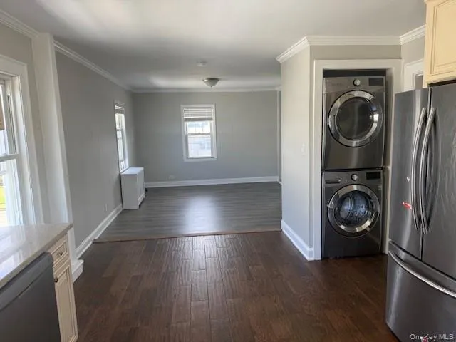 Washroom with ornamental molding, dark wood-type flooring, and stacked washer and clothes dryer Washroom with ornamental molding, dark wood-type flooring, and stacked washer and clothes dryer