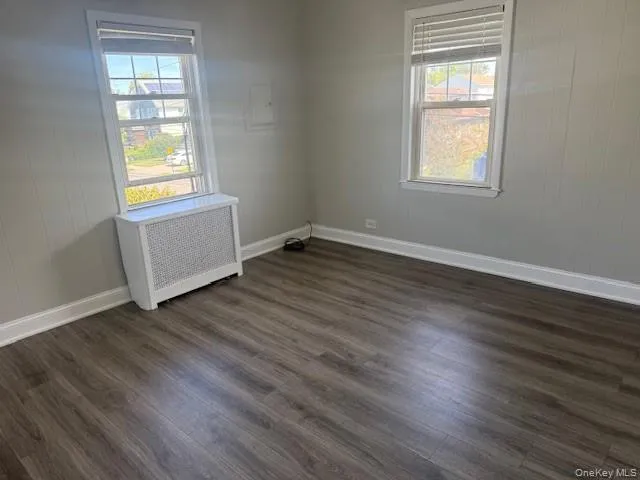 Empty room featuring radiator heating unit, dark wood finished floors, and wood walls Empty room featuring radiator heating unit, dark wood finished floors, and wood walls