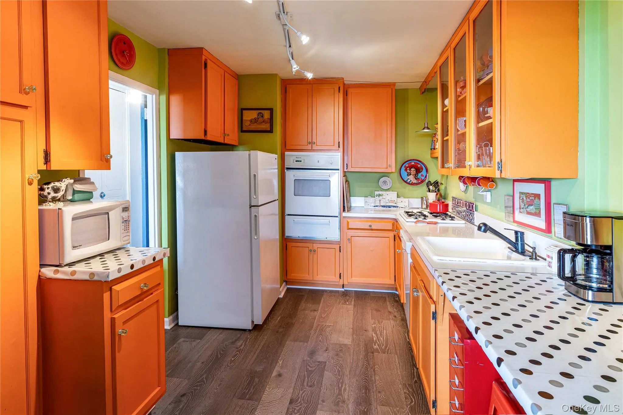 Kitchen featuring white appliances, a warming drawer, dark wood-style floors, glass insert cabinets, and track lighting Kitchen featuring white appliances, a warming drawer, dark wood-style floors, glass insert cabinets, and track lighting