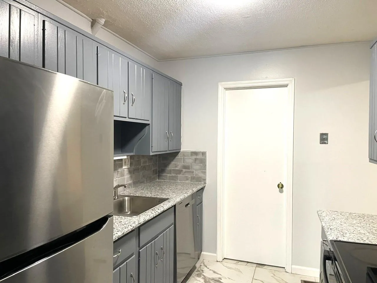 Kitchen with stainless steel appliances, gray cabinetry, decorative backsplash, light marble finish flooring, and a textured ceiling Kitchen with stainless steel appliances, gray cabinetry, decorative backsplash, light marble finish flooring, and a textured ceiling