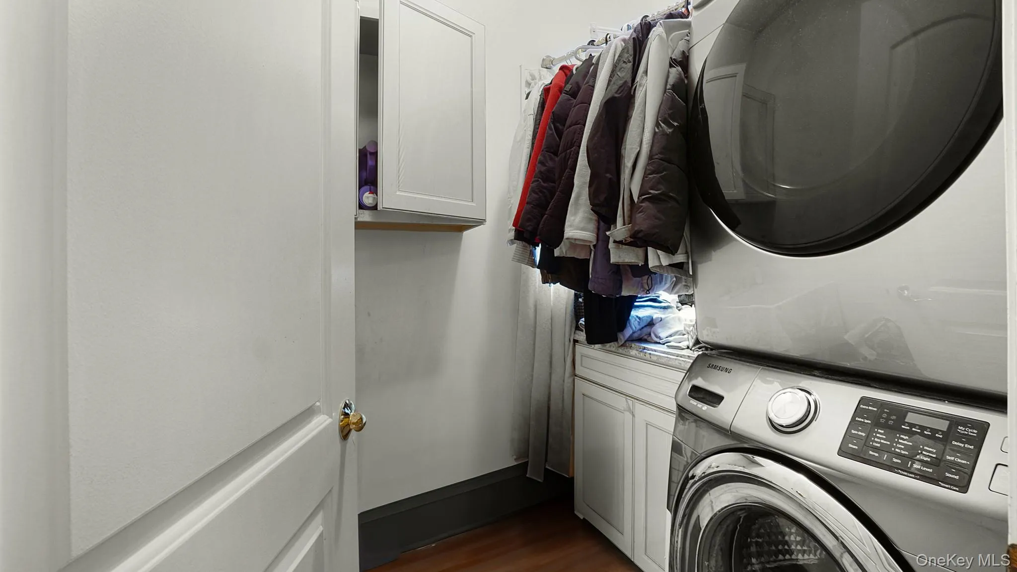 Laundry area with stacked washer and clothes dryer, cabinet space, and dark wood-type flooring Laundry area with stacked washer and clothes dryer, cabinet space, and dark wood-type flooring