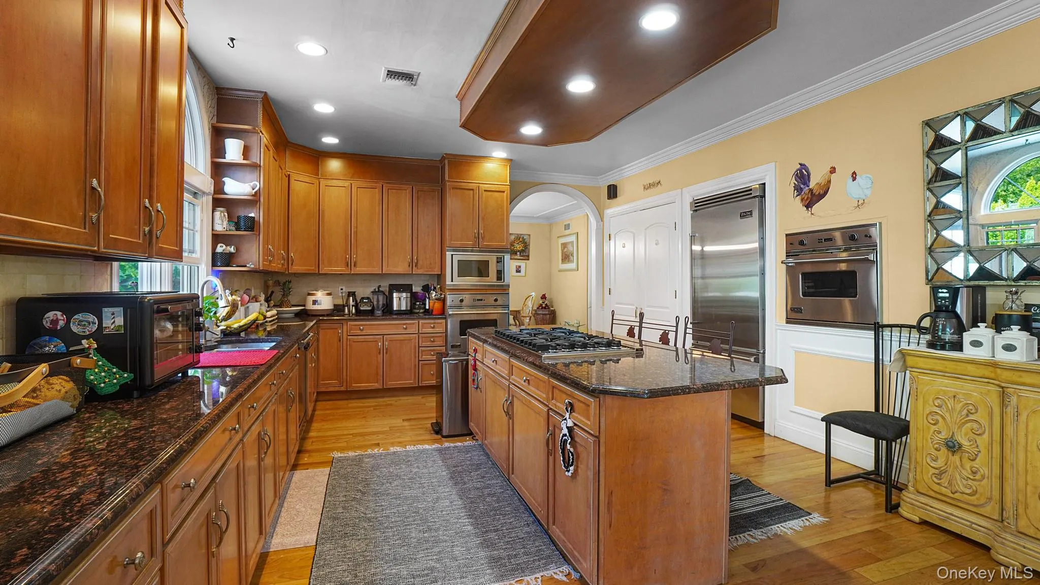 Kitchen featuring stainless steel appliances, open shelves, light wood-style floors, a kitchen island, and arched walkways Kitchen featuring stainless steel appliances, open shelves, light wood-style floors, a kitchen island, and arched walkways