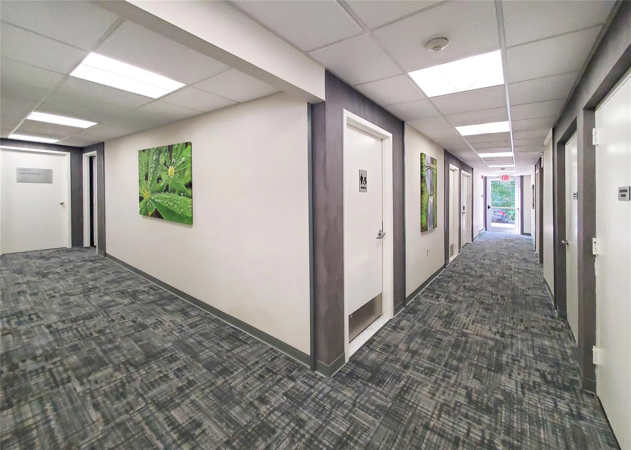 Hallway featuring a paneled ceiling and dark carpet Hallway featuring a paneled ceiling and dark carpet