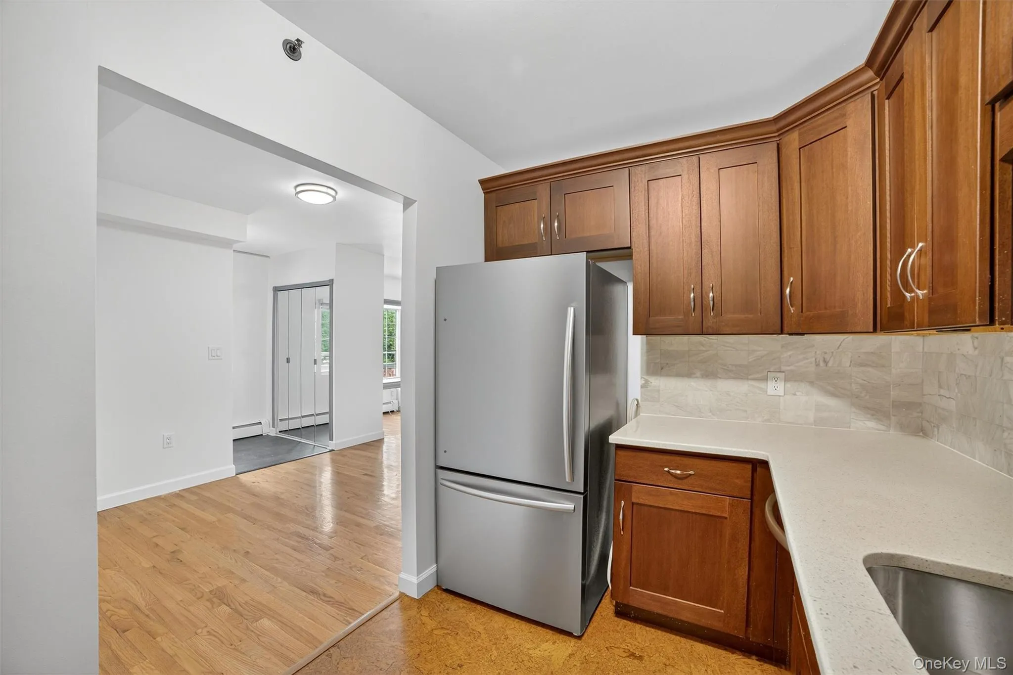 Kitchen with freestanding refrigerator, backsplash, brown cabinetry, and baseboard heating Kitchen with freestanding refrigerator, backsplash, brown cabinetry, and baseboard heating