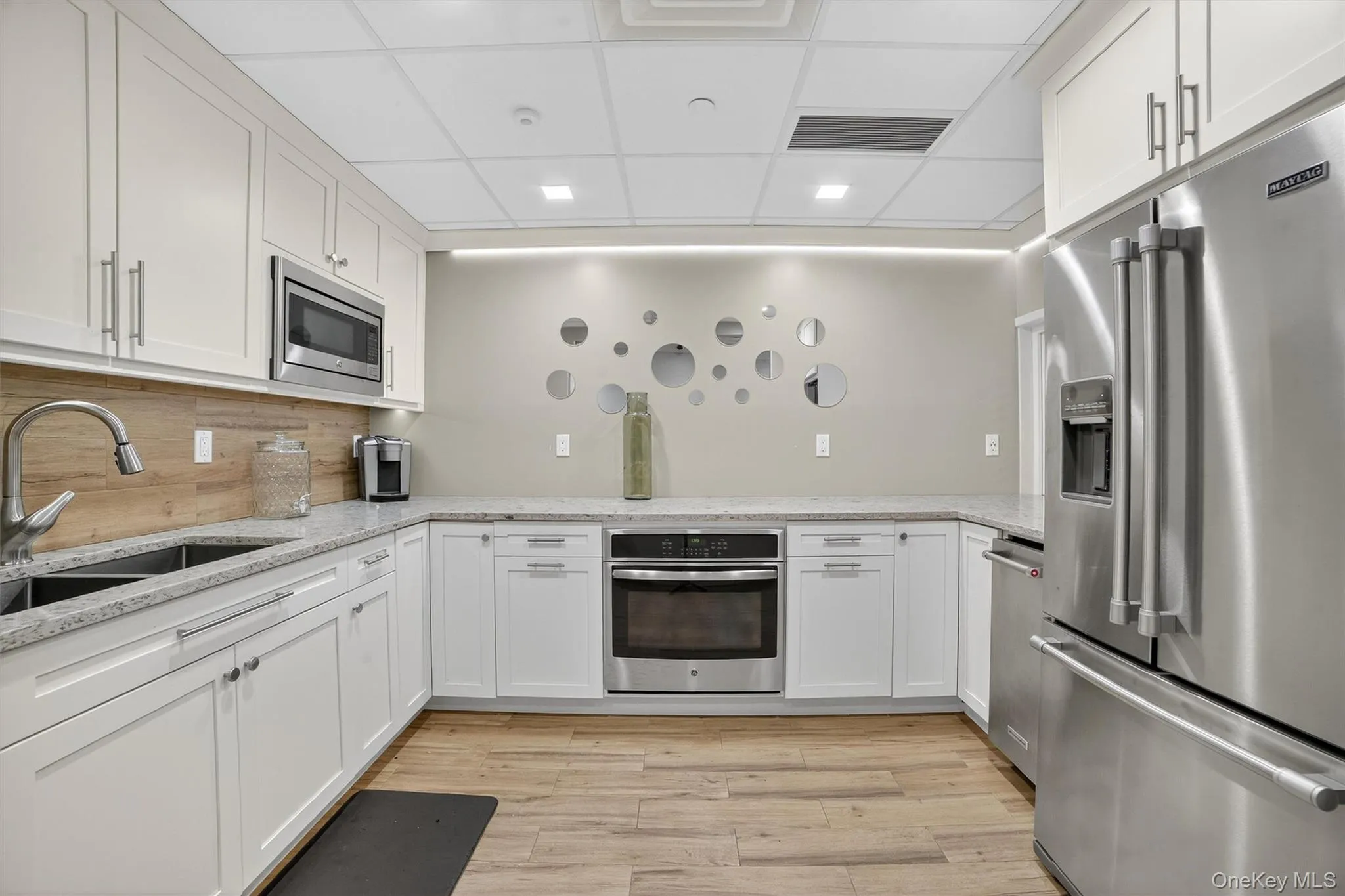 Community kitchen Kitchen featuring stainless steel appliances, a drop ceiling, light wood finished floors, white cabinetry, and light stone countertops Community kitchen Kitchen featuring stainless steel appliances, a drop ceiling, light wood finished floors, white cabinetry, and light stone countertops