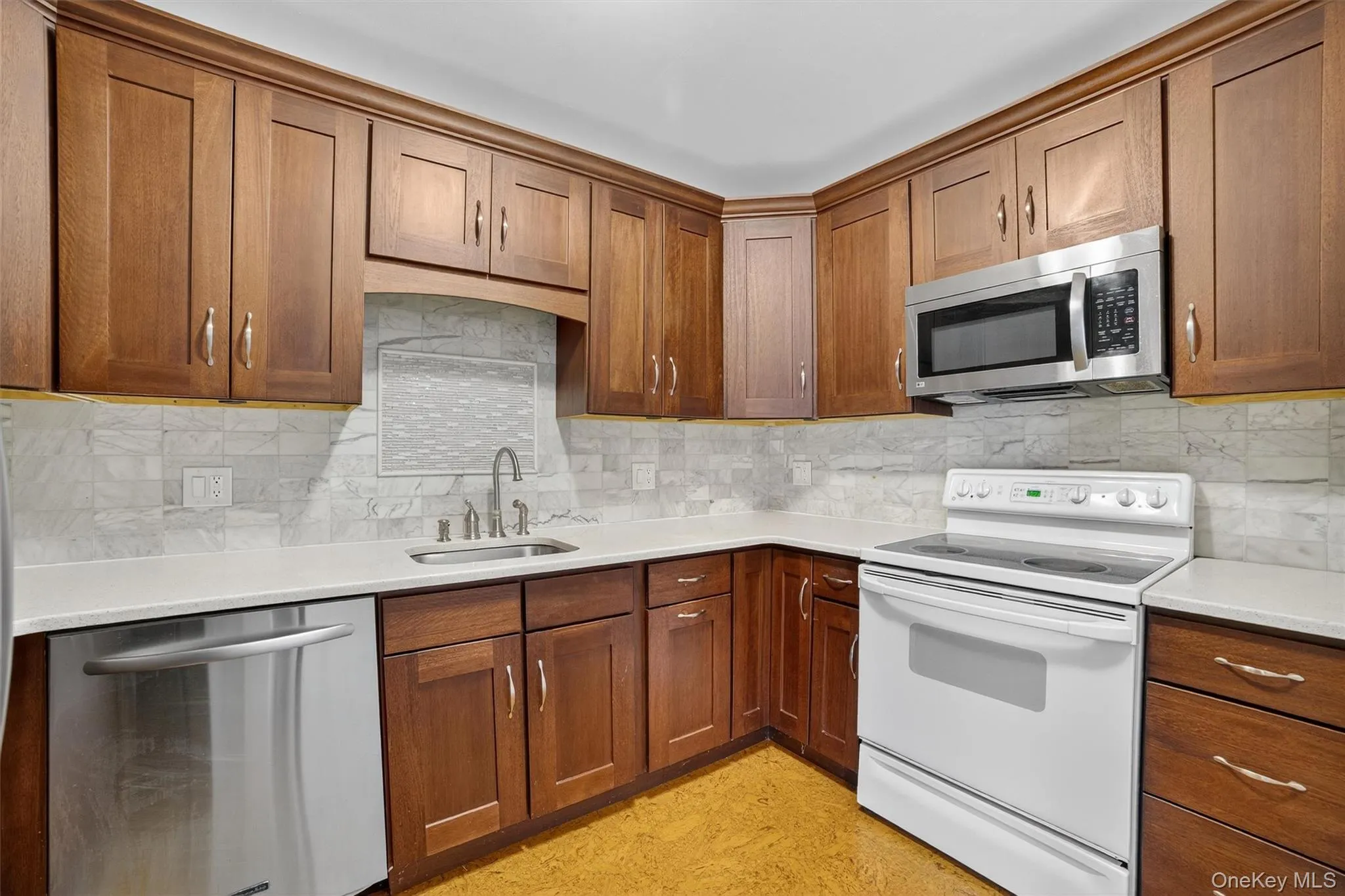 Kitchen featuring stainless steel appliances, tasteful backsplash, light countertops, and brown cabinetry Kitchen featuring stainless steel appliances, tasteful backsplash, light countertops, and brown cabinetry