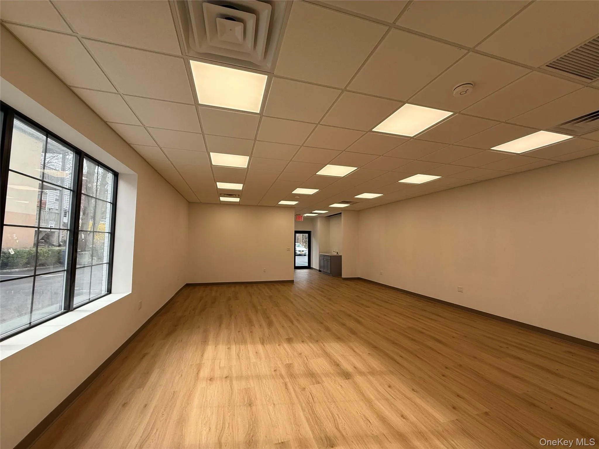 Empty room featuring light wood finished floors, a smoke detector, and a drop ceiling Empty room featuring light wood finished floors, a smoke detector, and a drop ceiling