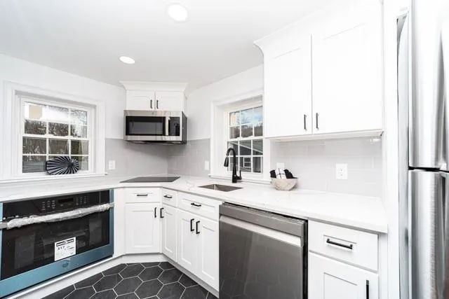 Kitchen with stainless steel appliances, light countertops, white cabinets, tasteful backsplash, and dark tile patterned flooring Kitchen with stainless steel appliances, light countertops, white cabinets, tasteful backsplash, and dark tile patterned flooring