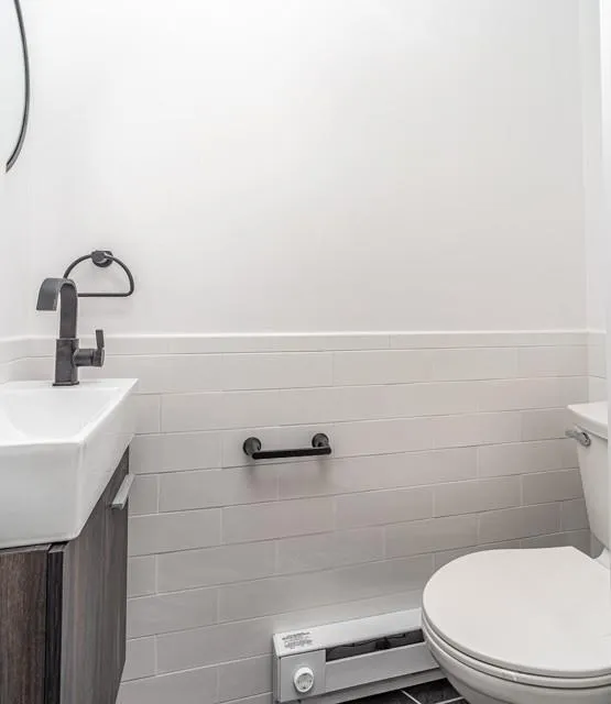 Half bath featuring tile walls, vanity, a wainscoted wall, and a baseboard heating unit Half bath featuring tile walls, vanity, a wainscoted wall, and a baseboard heating unit