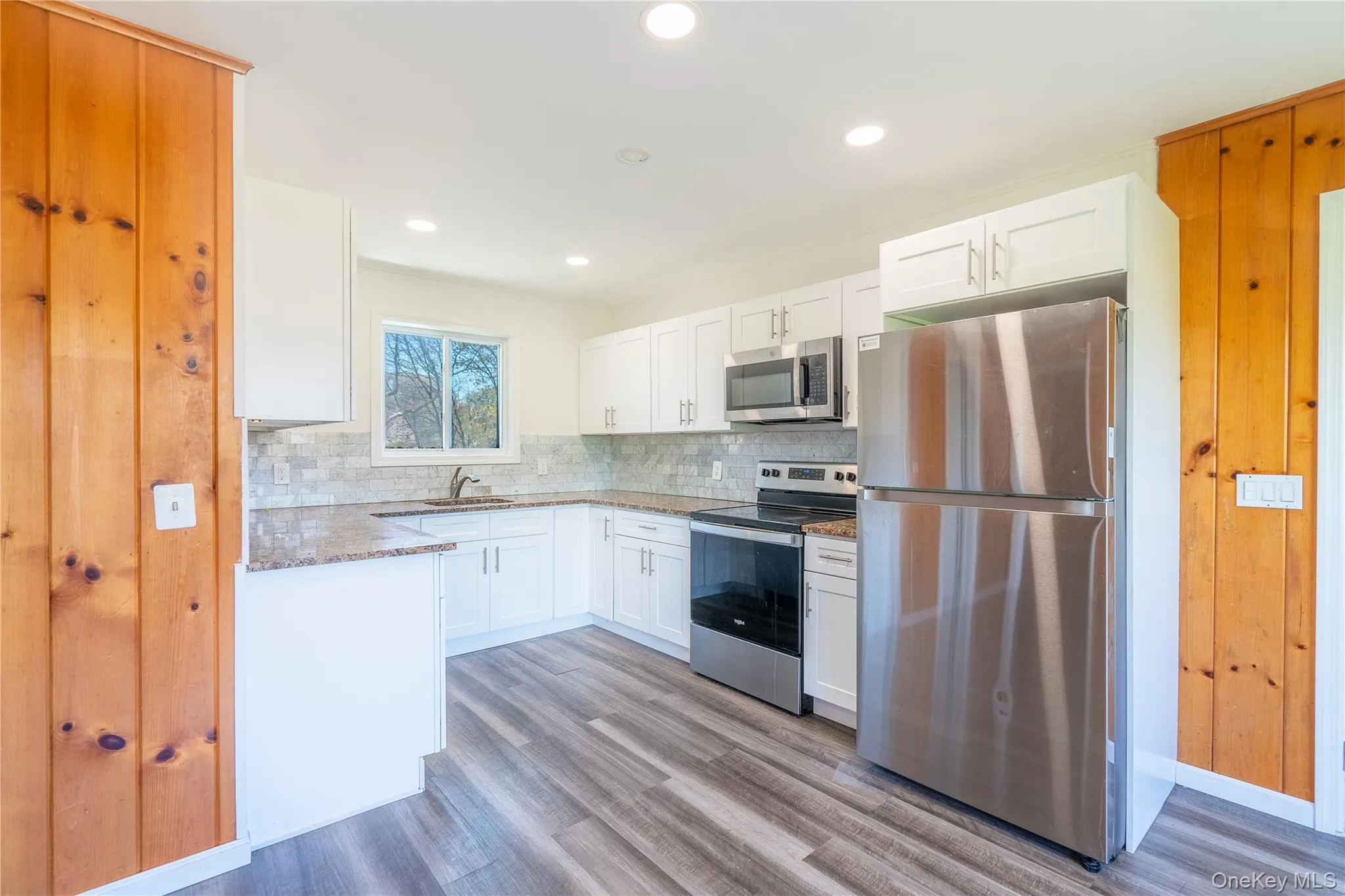 Kitchen featuring appliances with stainless steel finishes, light stone countertops, tasteful backsplash, light wood-style flooring, and white cabinetry Kitchen featuring appliances with stainless steel finishes, light stone countertops, tasteful backsplash, light wood-style flooring, and white cabinetry