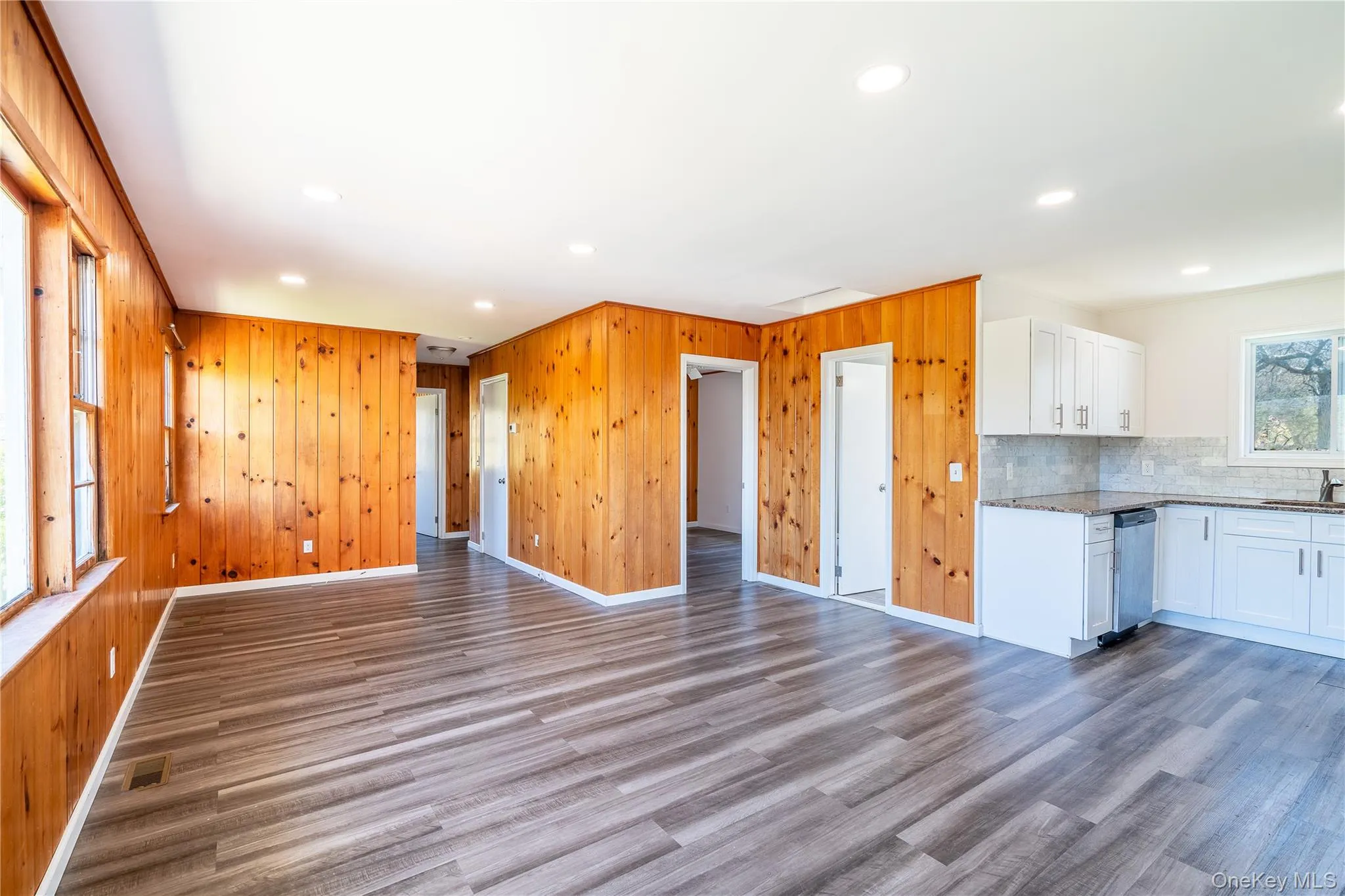Kitchen featuring open floor plan, stainless steel dishwasher, wood finished floors, light stone counters, and backsplash Kitchen featuring open floor plan, stainless steel dishwasher, wood finished floors, light stone counters, and backsplash