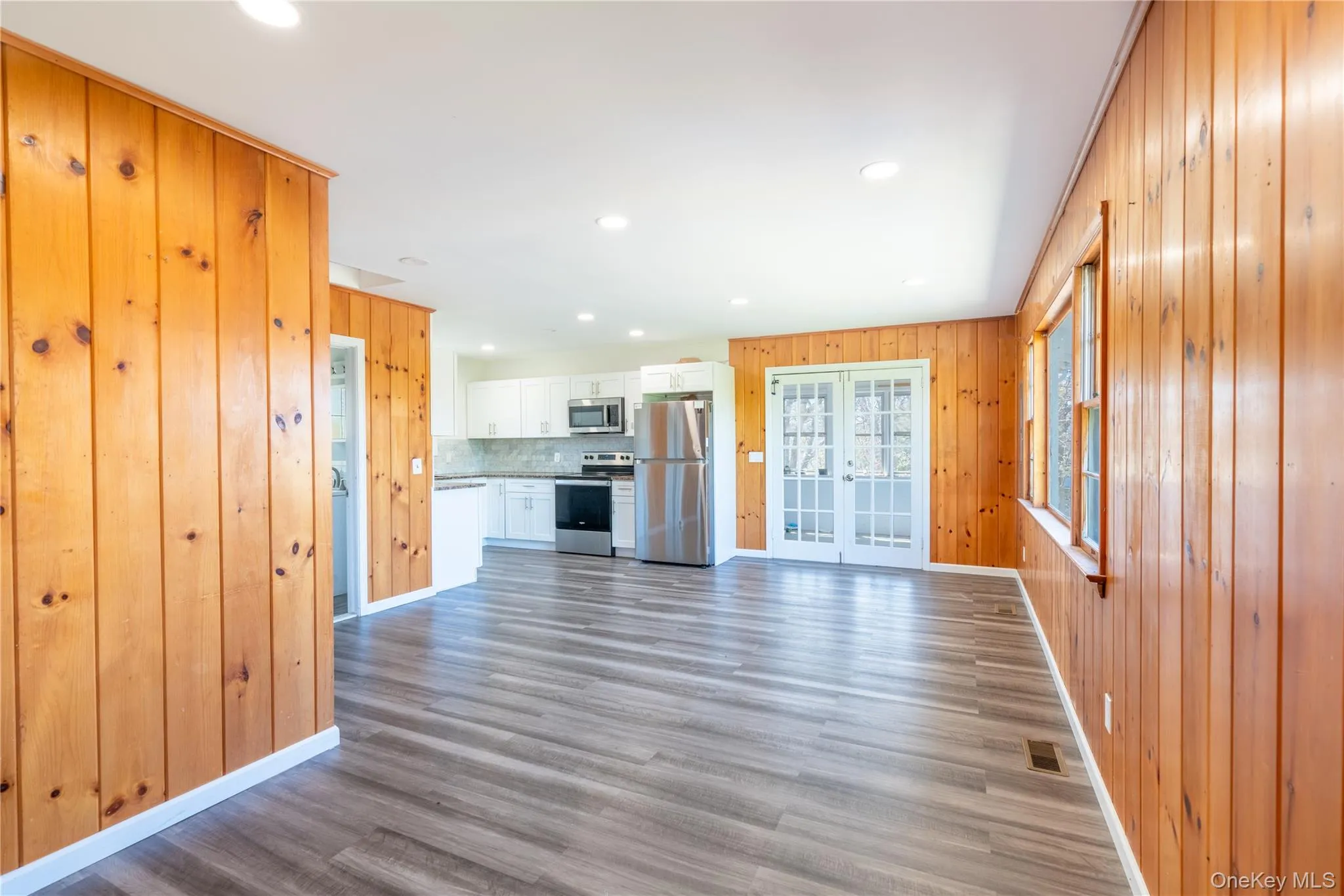 Unfurnished living room featuring french doors, wooden walls, wood finished floors, and recessed lighting Unfurnished living room featuring french doors, wooden walls, wood finished floors, and recessed lighting