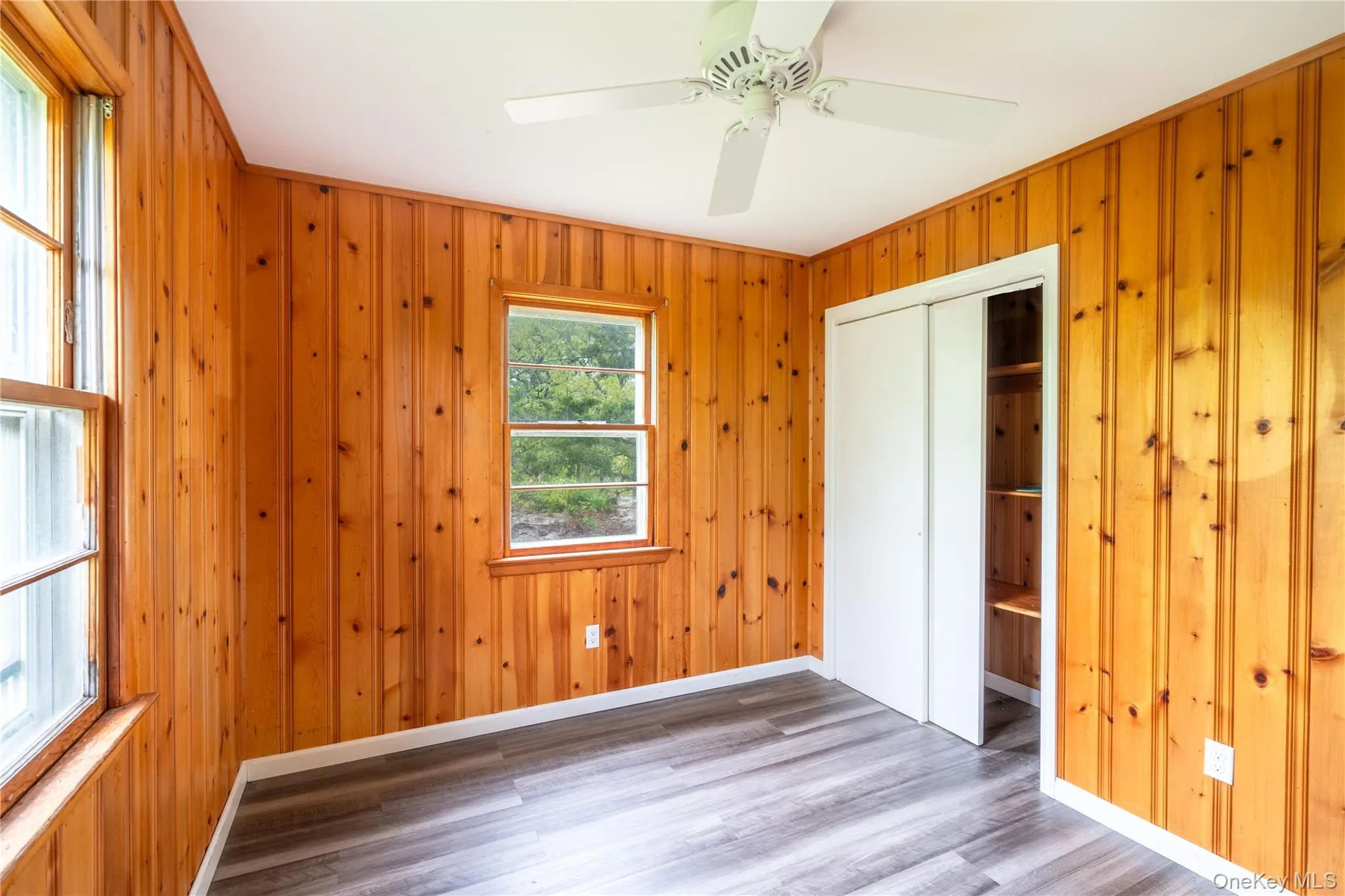 Unfurnished bedroom with wood finished floors, a closet, ceiling fan, and wooden walls Unfurnished bedroom with wood finished floors, a closet, ceiling fan, and wooden walls
