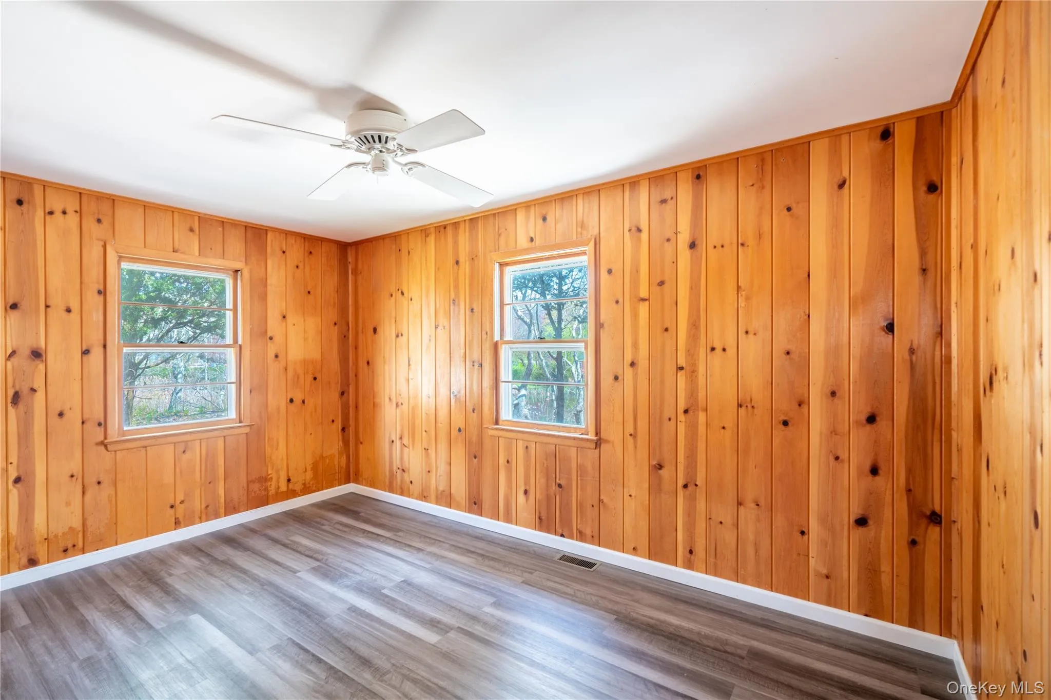 Spare room featuring wood finished floors, plenty of natural light, ceiling fan, and wood walls Spare room featuring wood finished floors, plenty of natural light, ceiling fan, and wood walls