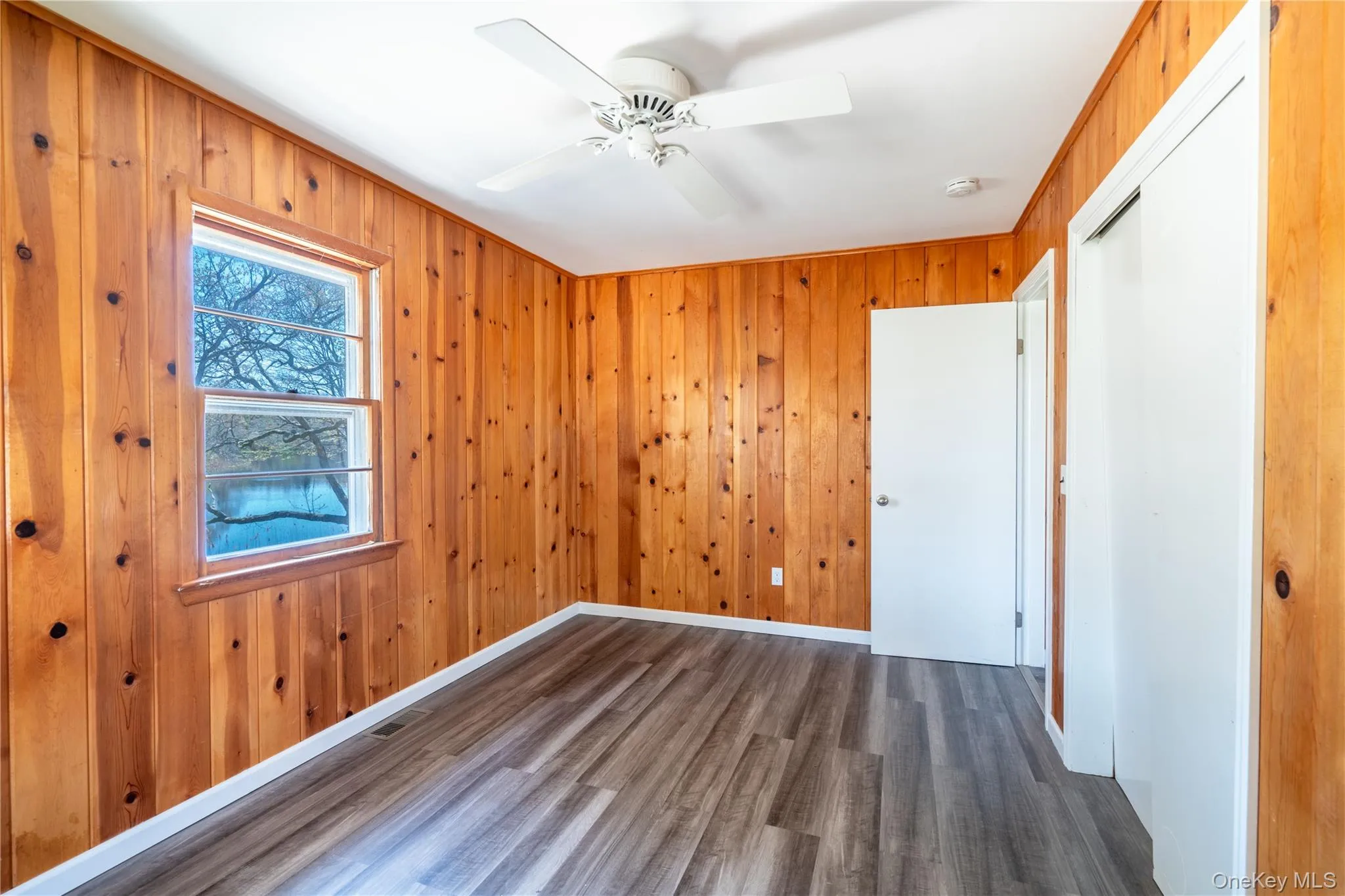 Unfurnished bedroom with wood finished floors, a closet, wood walls, and ceiling fan Unfurnished bedroom with wood finished floors, a closet, wood walls, and ceiling fan