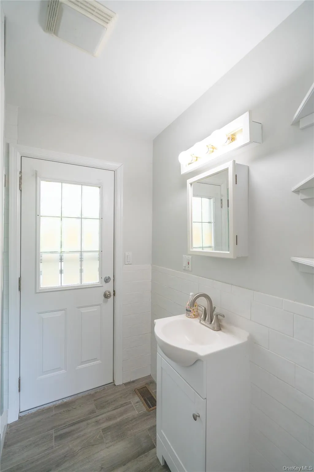 Bathroom featuring tile walls, vanity, wood finished floors, and wainscoting Bathroom featuring tile walls, vanity, wood finished floors, and wainscoting