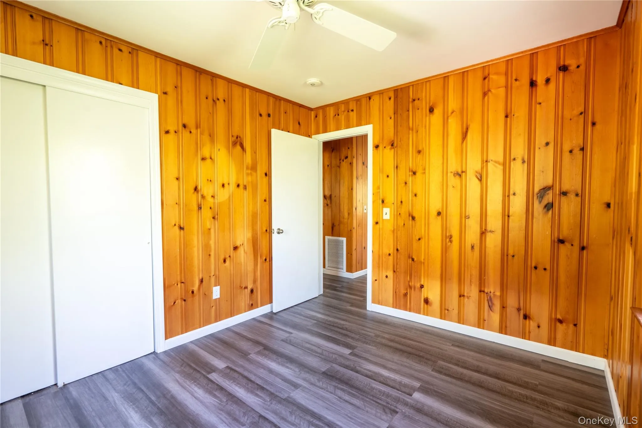 Unfurnished bedroom featuring dark wood-style flooring, a closet, wood walls, and ceiling fan Unfurnished bedroom featuring dark wood-style flooring, a closet, wood walls, and ceiling fan