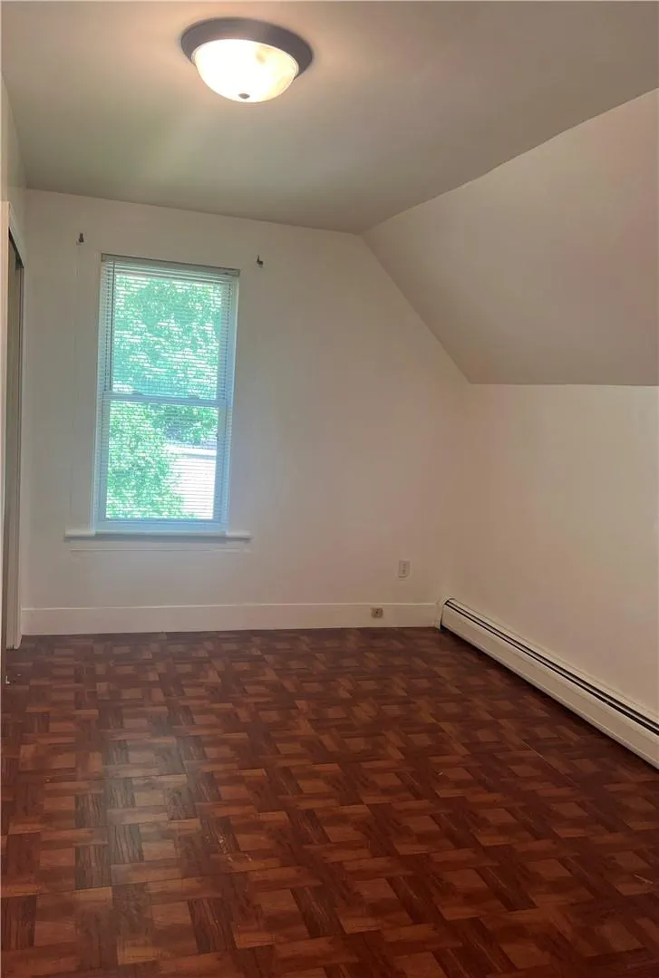 Bedroom featuring dark parquet flooring, a baseboard heating unit, and lofted ceiling Bedroom featuring dark parquet flooring, a baseboard heating unit, and lofted ceiling
