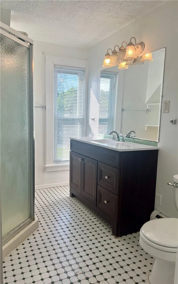 Bathroom featuring a textured ceiling, tile floors, an enclosed shower, vanity, and toilet Bathroom featuring a textured ceiling, tile floors, an enclosed shower, vanity, and toilet