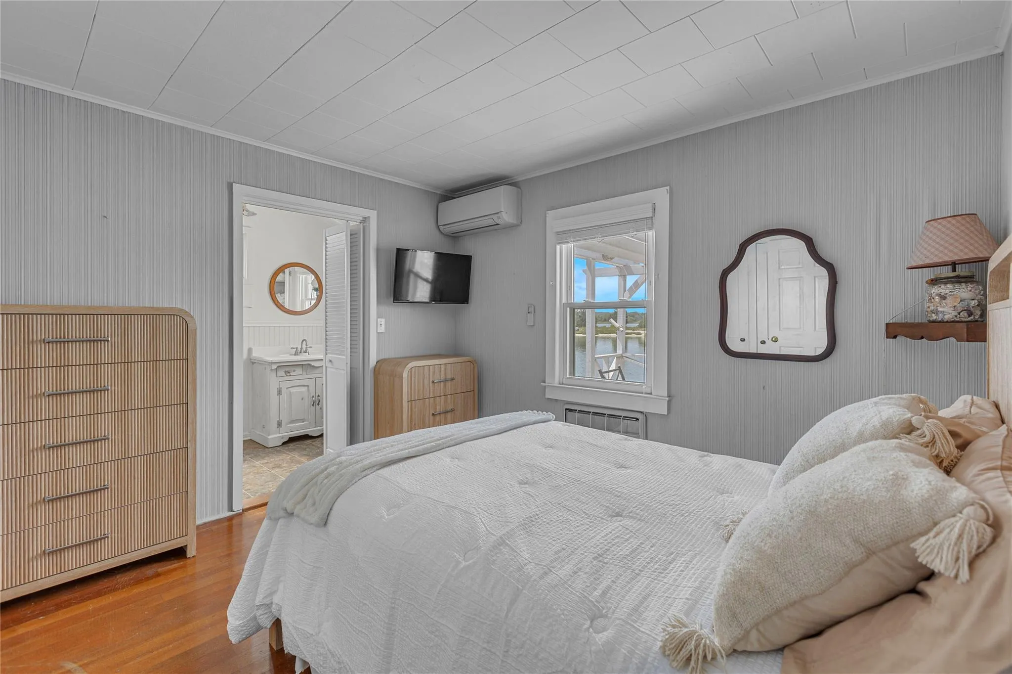Bedroom with crown molding, wood finished floors, a wall mounted air conditioner, and ensuite bath Bedroom with crown molding, wood finished floors, a wall mounted air conditioner, and ensuite bath