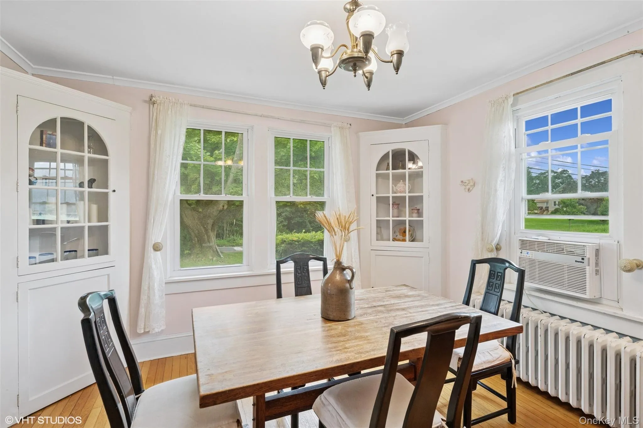 Dining room featuring radiator heating unit, a chandelier, ornamental molding, cooling unit, and light wood-style floors Dining room featuring radiator heating unit, a chandelier, ornamental molding, cooling unit, and light wood-style floors