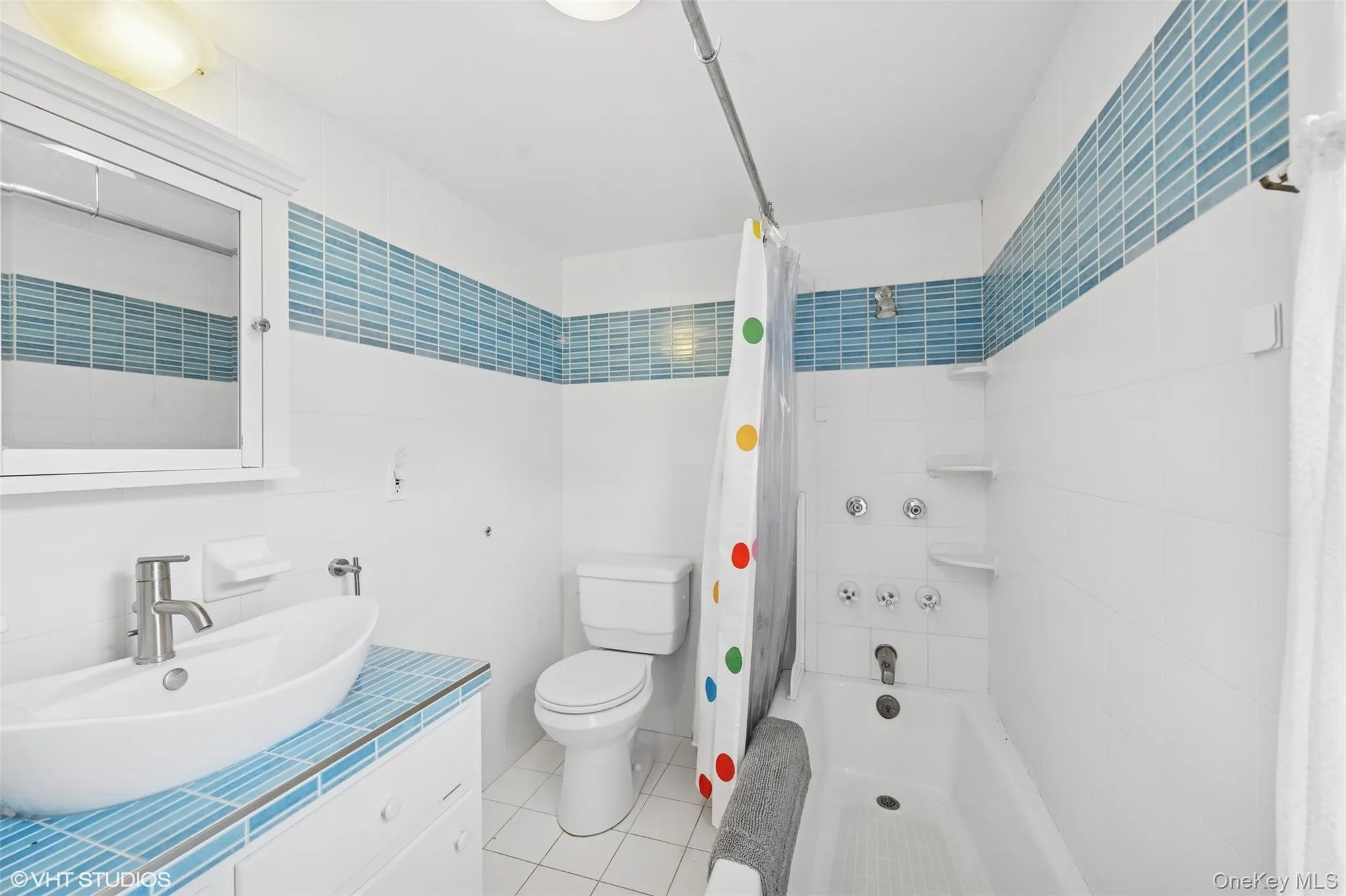 Full bathroom featuring tile walls, shower / bath combo with shower curtain, tile patterned flooring, and vanity Full bathroom featuring tile walls, shower / bath combo with shower curtain, tile patterned flooring, and vanity