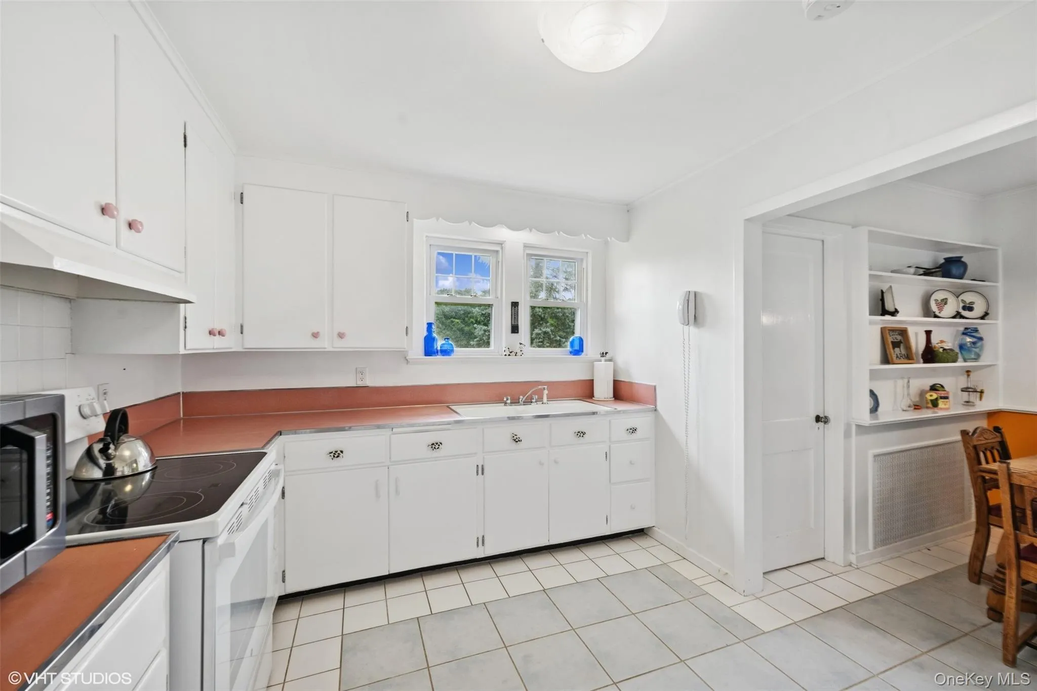 Kitchen featuring white electric range, stainless steel microwave, white cabinetry, light tile patterned flooring, and crown molding Kitchen featuring white electric range, stainless steel microwave, white cabinetry, light tile patterned flooring, and crown molding