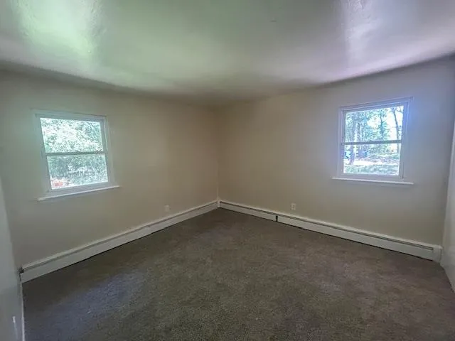Empty room with plenty of natural light, a baseboard heating unit, dark colored carpet, and baseboard heating Empty room with plenty of natural light, a baseboard heating unit, dark colored carpet, and baseboard heating