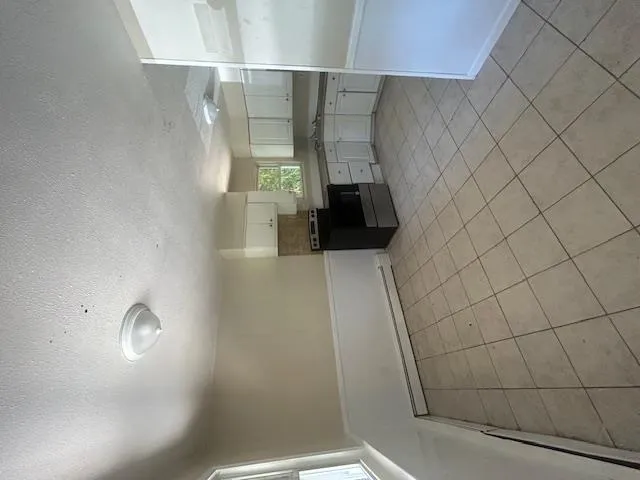 Kitchen with stove, white cabinets, baseboard heating, light tile patterned floors, and a textured ceiling Kitchen with stove, white cabinets, baseboard heating, light tile patterned floors, and a textured ceiling