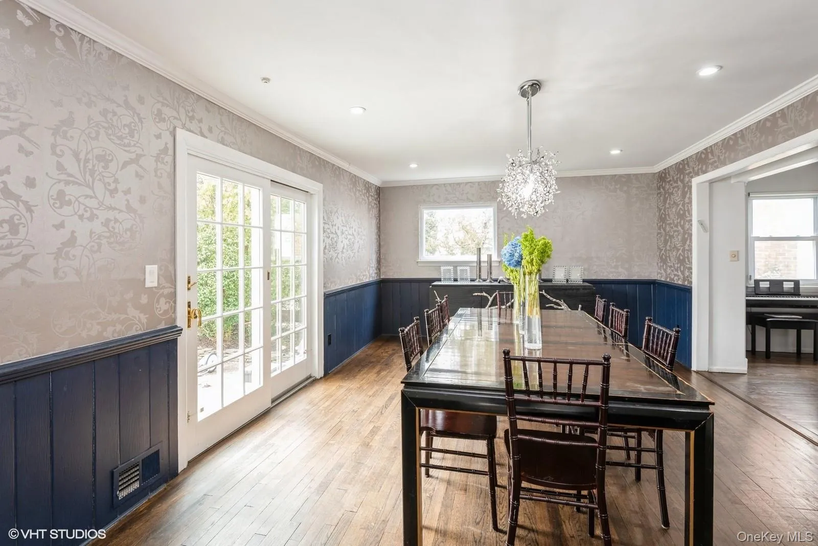 Dining room featuring a wainscoted wall, wallpapered walls, a chandelier, hardwood / wood-style floors, and crown molding Dining room featuring a wainscoted wall, wallpapered walls, a chandelier, hardwood / wood-style floors, and crown molding