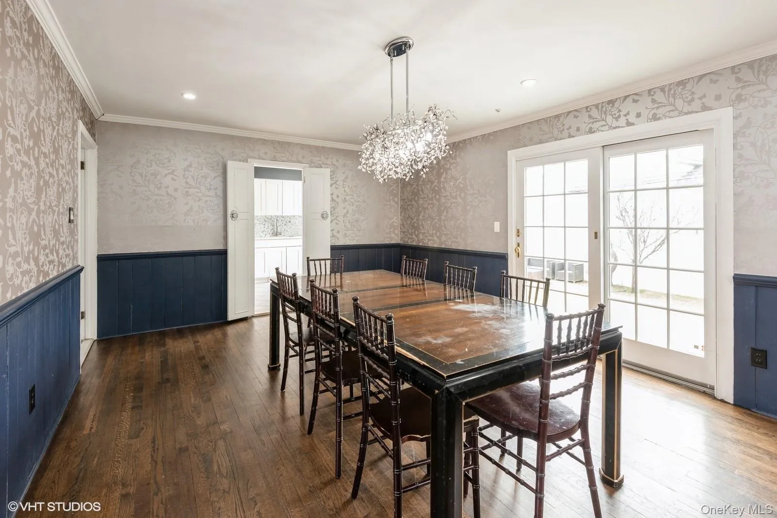 Dining room featuring wallpapered walls, wainscoting, crown molding, a chandelier, and hardwood / wood-style floors Dining room featuring wallpapered walls, wainscoting, crown molding, a chandelier, and hardwood / wood-style floors