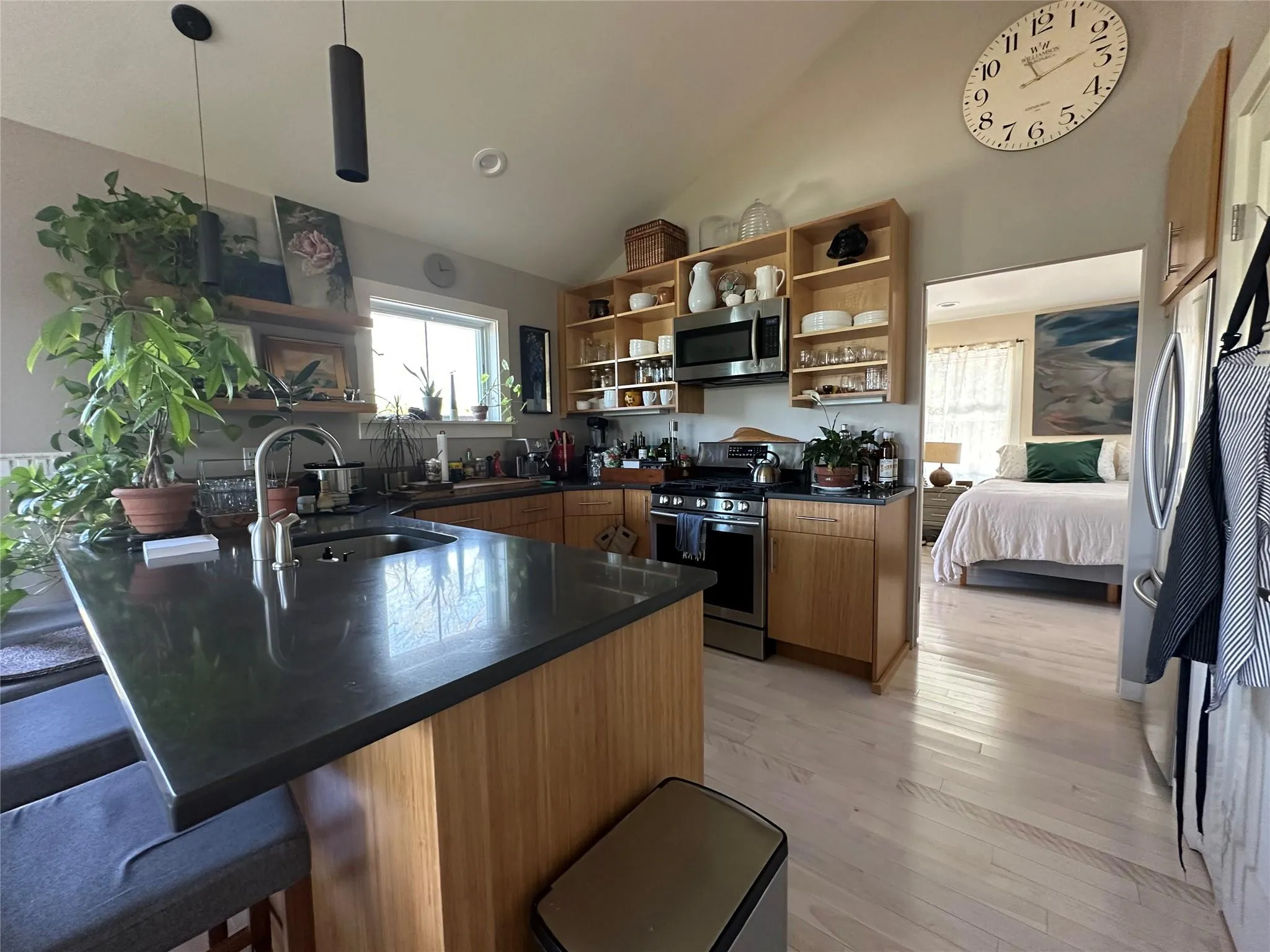 Kitchen featuring open shelves, appliances with stainless steel finishes, dark countertops, a peninsula, and a kitchen bar Kitchen featuring open shelves, appliances with stainless steel finishes, dark countertops, a peninsula, and a kitchen bar