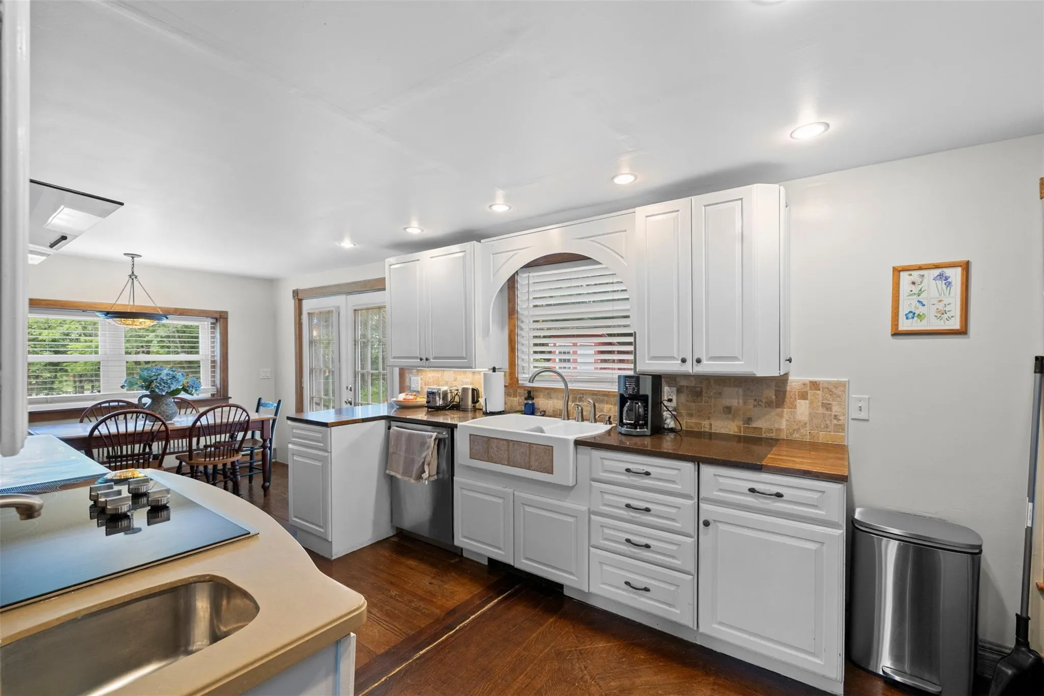 Kitchen featuring stainless steel dishwasher, recessed lighting, backsplash, white cabinetry, and dark wood-style flooring Kitchen featuring stainless steel dishwasher, recessed lighting, backsplash, white cabinetry, and dark wood-style flooring