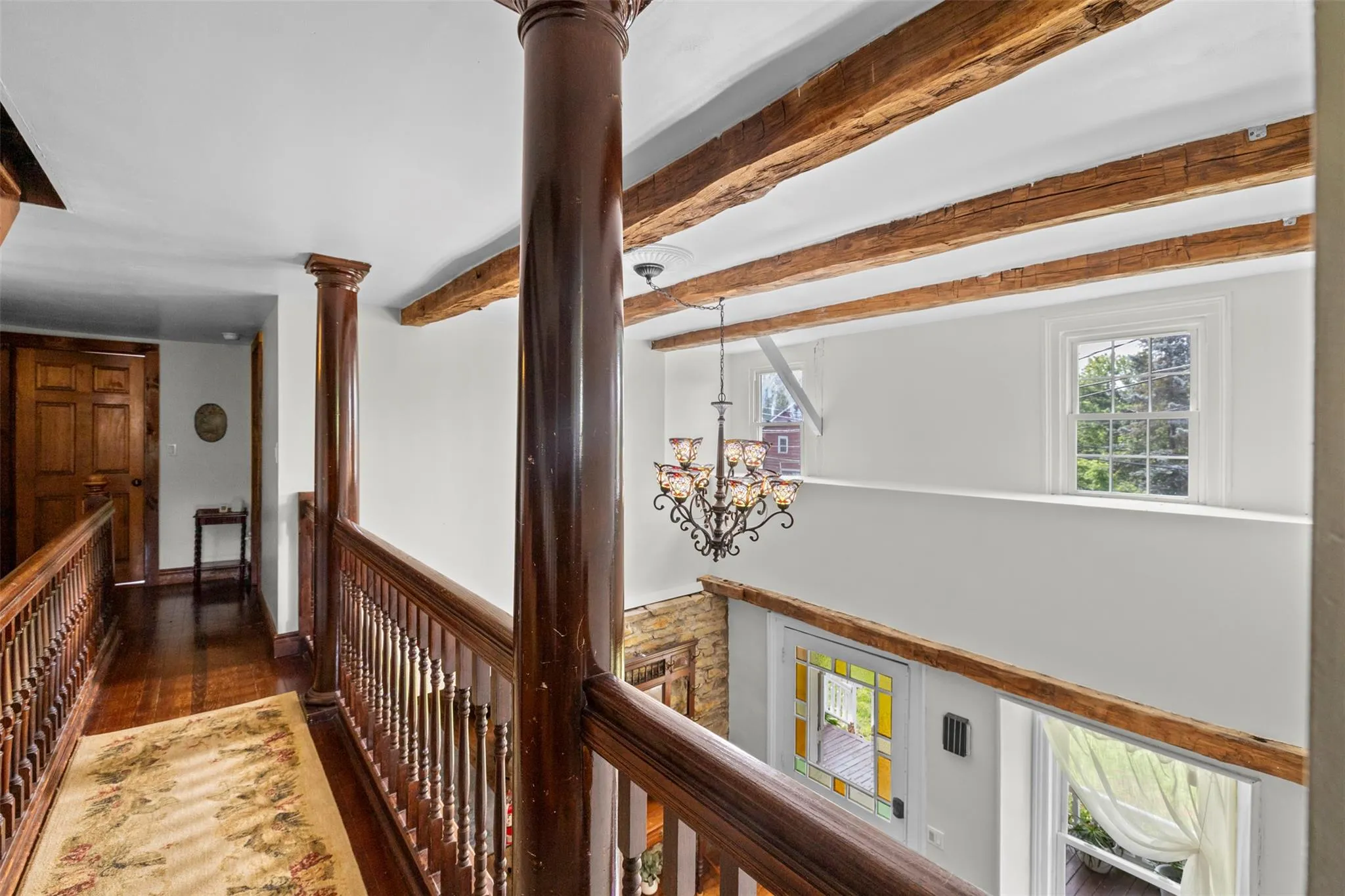 Hall featuring an upstairs landing, wood finished floors, a chandelier, decorative columns, and beamed ceiling Hall featuring an upstairs landing, wood finished floors, a chandelier, decorative columns, and beamed ceiling