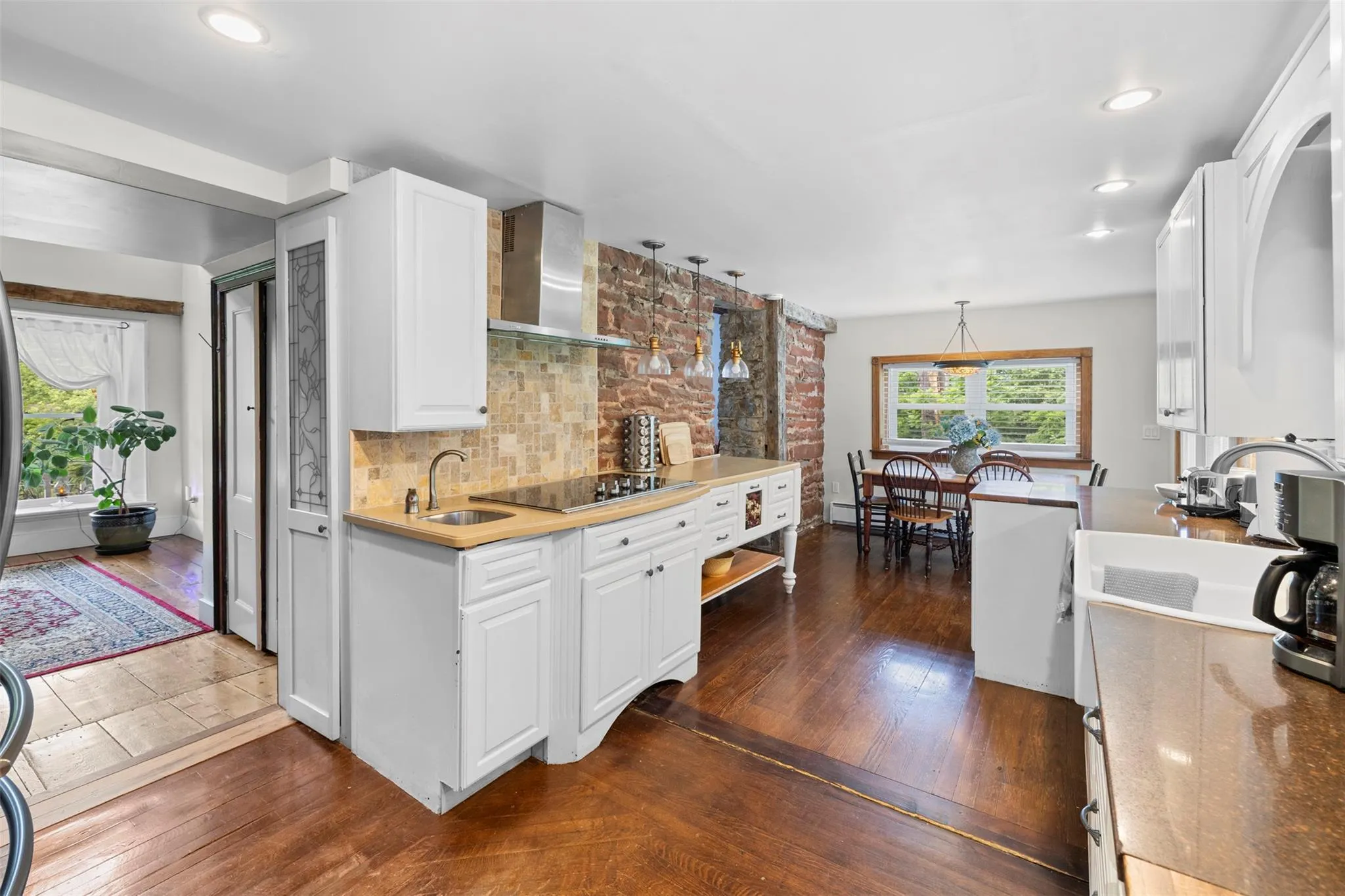 Kitchen with wall chimney exhaust hood, black electric stovetop, white cabinets, backsplash, and recessed lighting Kitchen with wall chimney exhaust hood, black electric stovetop, white cabinets, backsplash, and recessed lighting