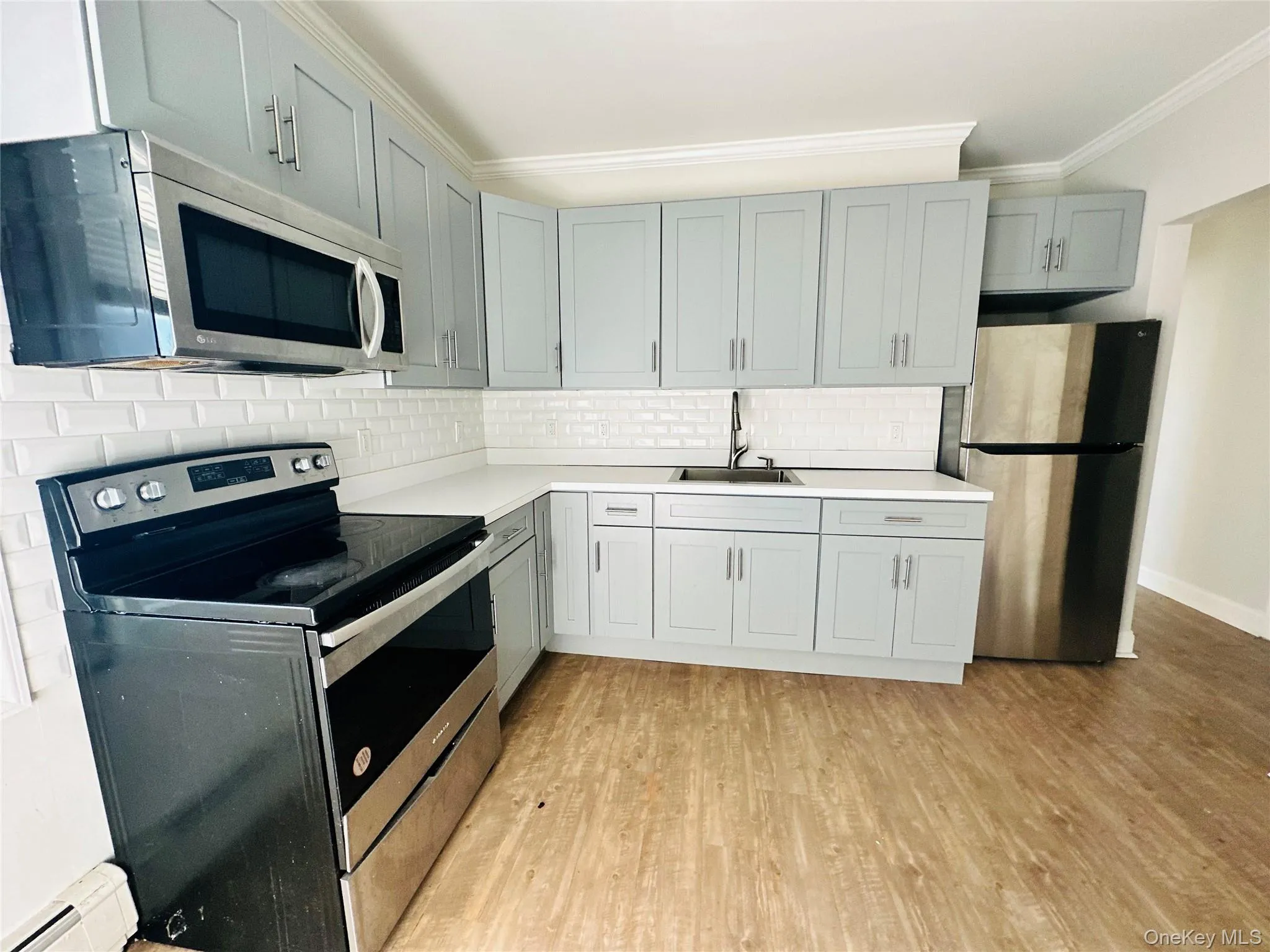 Kitchen featuring decorative backsplash, appliances with stainless steel finishes, ornamental molding, sink, and light hardwood / wood-style flooring Kitchen featuring decorative backsplash, appliances with stainless steel finishes, ornamental molding, sink, and light hardwood / wood-style flooring