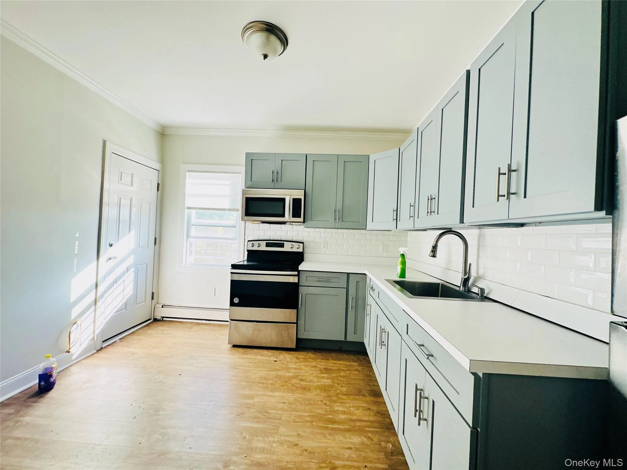 Kitchen featuring sink, light hardwood / wood-style flooring, ornamental molding, a baseboard radiator, and stainless steel appliances Kitchen featuring sink, light hardwood / wood-style flooring, ornamental molding, a baseboard radiator, and stainless steel appliances