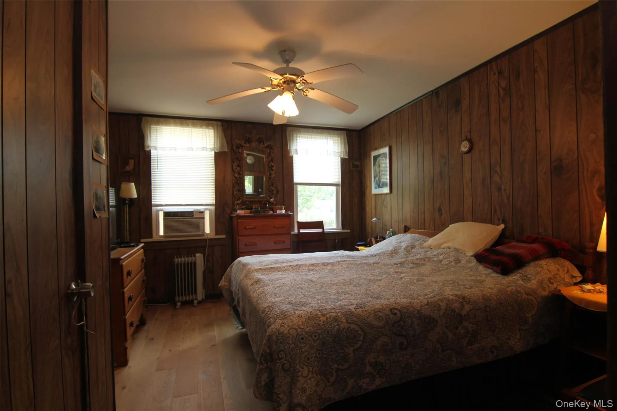Bedroom with radiator heating unit, light wood-type flooring, cooling unit, wood walls, and ceiling fan Bedroom with radiator heating unit, light wood-type flooring, cooling unit, wood walls, and ceiling fan