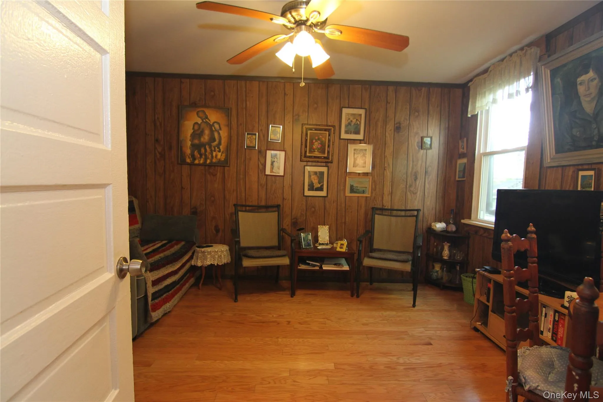 Living area with ceiling fan, wood walls, and light wood finished floors Living area with ceiling fan, wood walls, and light wood finished floors