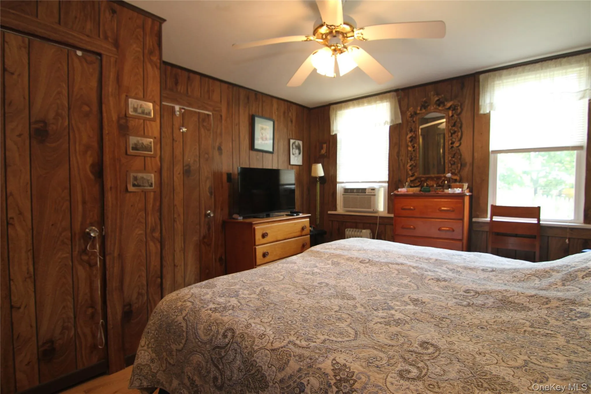 Bedroom with cooling unit, wood walls, multiple windows, and ceiling fan Bedroom with cooling unit, wood walls, multiple windows, and ceiling fan