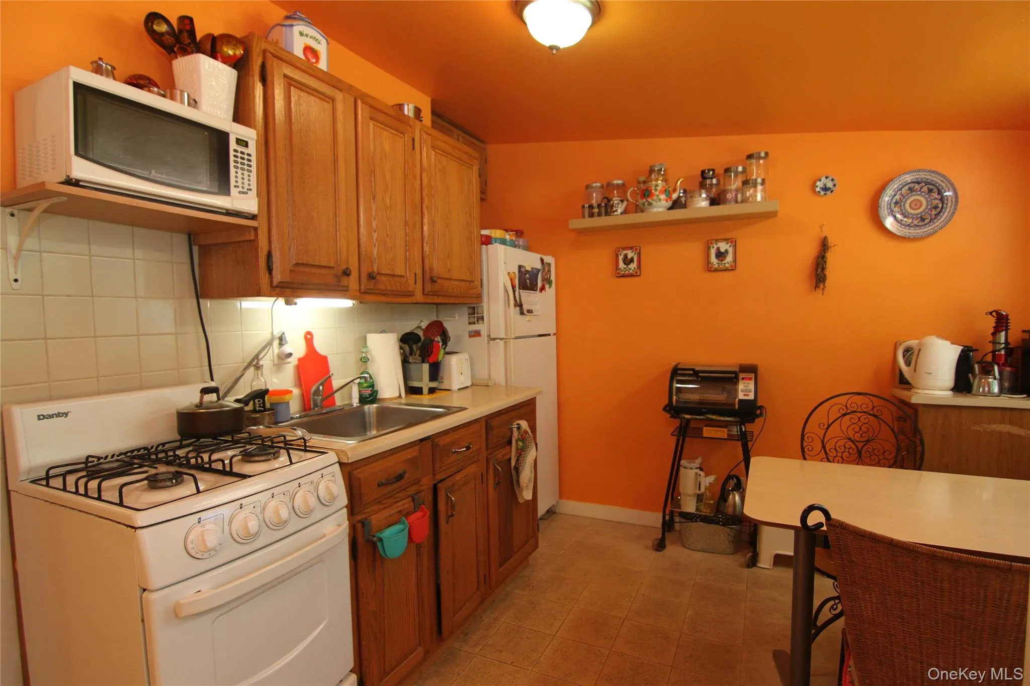 Kitchen with white appliances, light countertops, decorative backsplash, and brown cabinets Kitchen with white appliances, light countertops, decorative backsplash, and brown cabinets