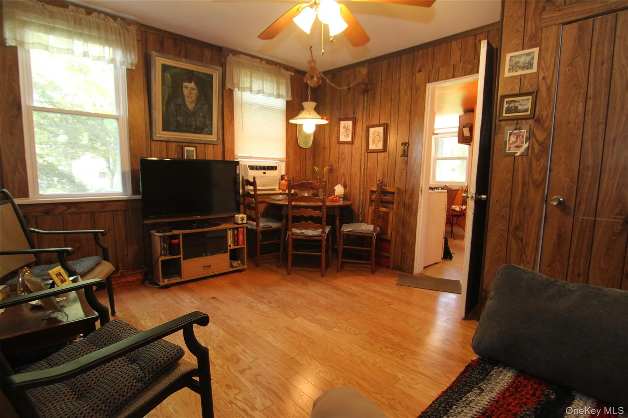 Living area with wood walls, ceiling fan, and light wood-style flooring Living area with wood walls, ceiling fan, and light wood-style flooring